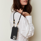 Person holding a black phone case with a strap against a neutral background