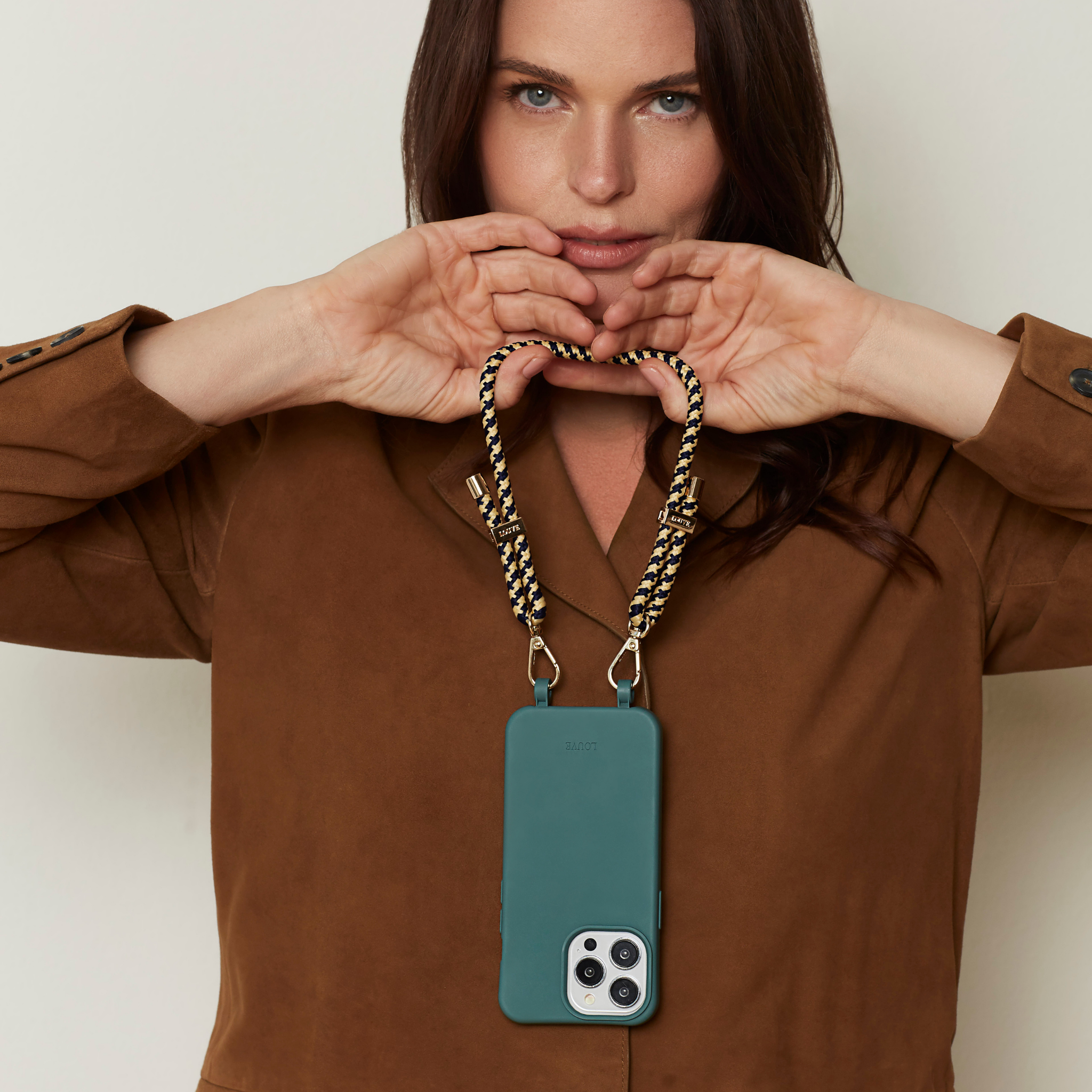 Woman holding a teal phone case with a gold chain strap against a neutral background