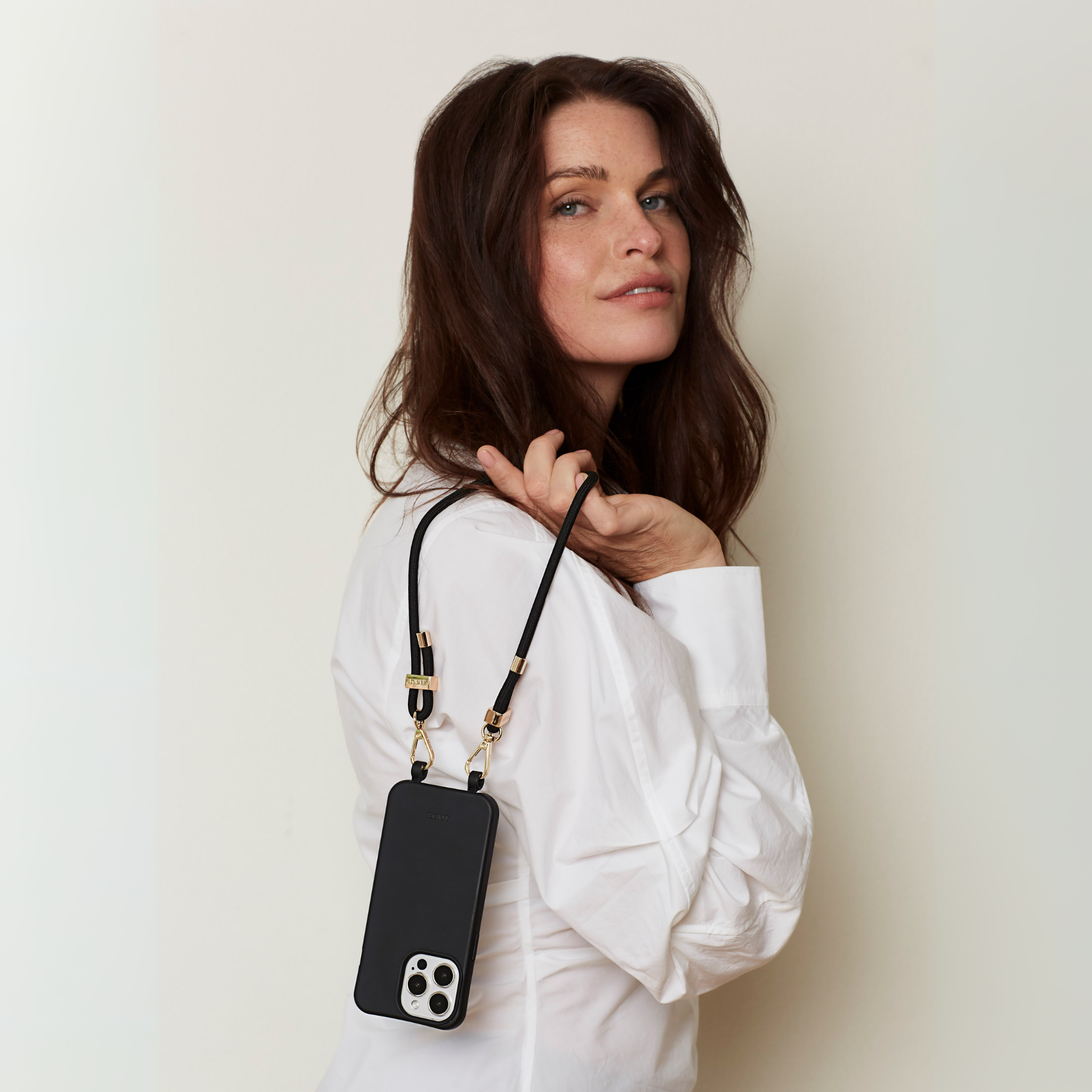 Woman holding a black phone case with a strap against a plain background